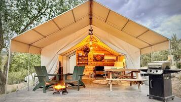 A tent with a wooden interior, a fire pit, and a grill outside.