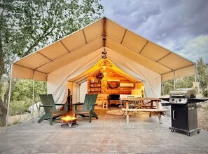 A tent with a wooden interior, a fire pit, and a grill outside.