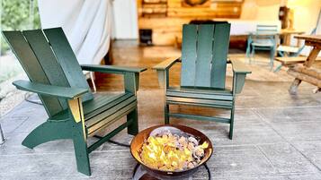 Two green Adirondack chairs, a campfire, and a tent interior with wooden walls and a hanging light fixture.