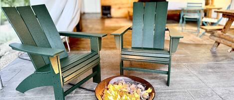 Two green Adirondack chairs, a campfire, and a tent interior with wooden walls and a hanging light fixture.