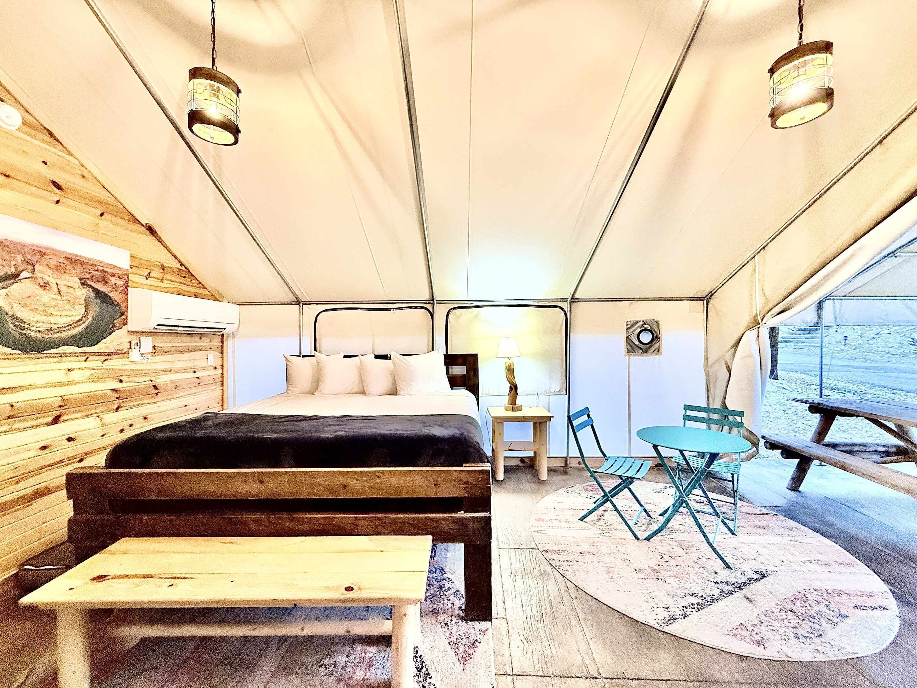 A tented room with a bed, a table, chairs, and a bench.
