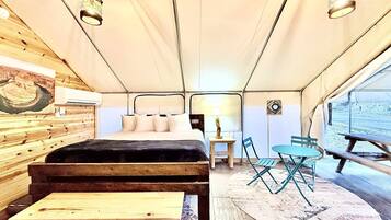 A tented room with a bed, a table, chairs, and a bench.
