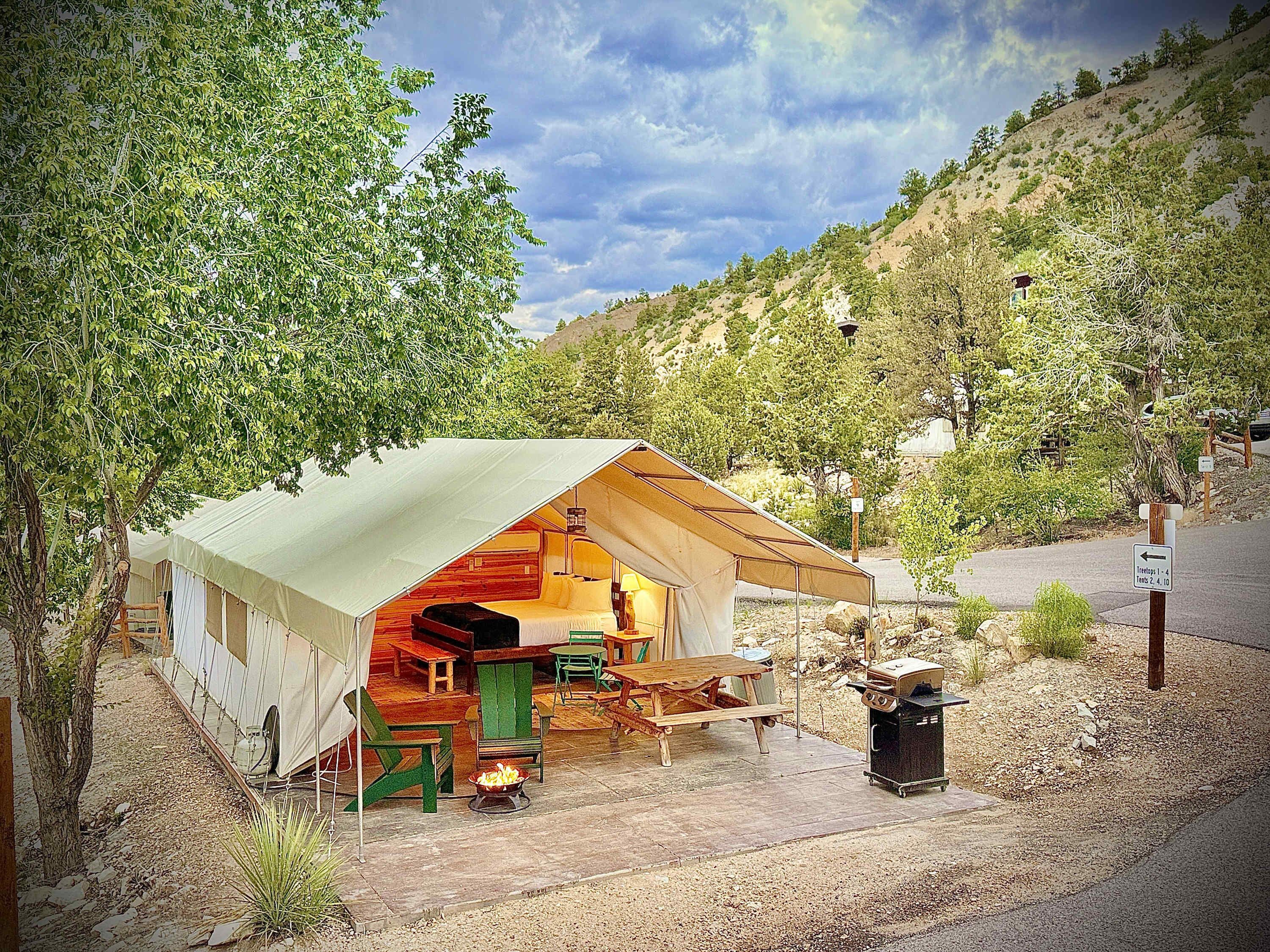 A tented accommodation with a dining area, a grill, and a view of the surrounding landscape.