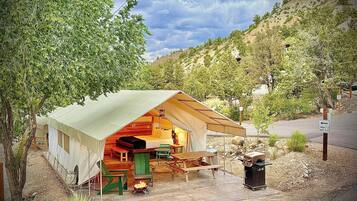 A tented accommodation with a dining area, a grill, and a view of the surrounding landscape.