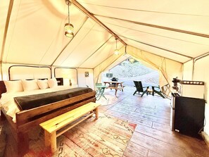 A tented accommodation with a bed, a bench, a table, chairs, and a speaker.
