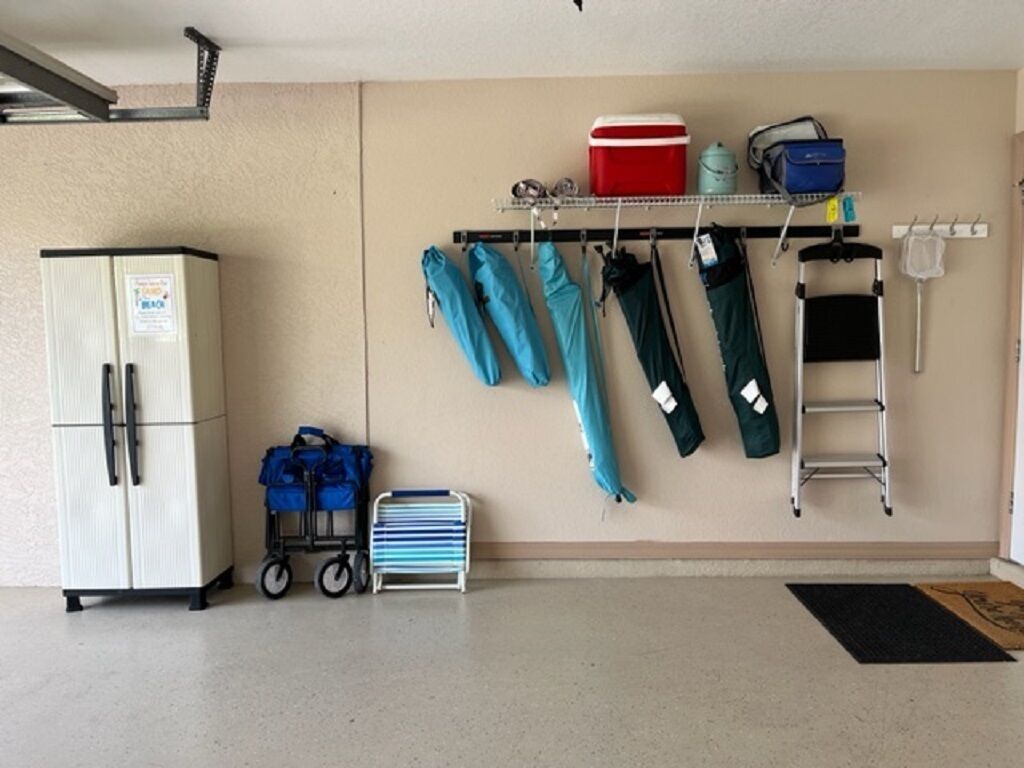 Een garage met een koelkast, een kar en een wandrek met diverse spullen, zoals tassen en een ladder.