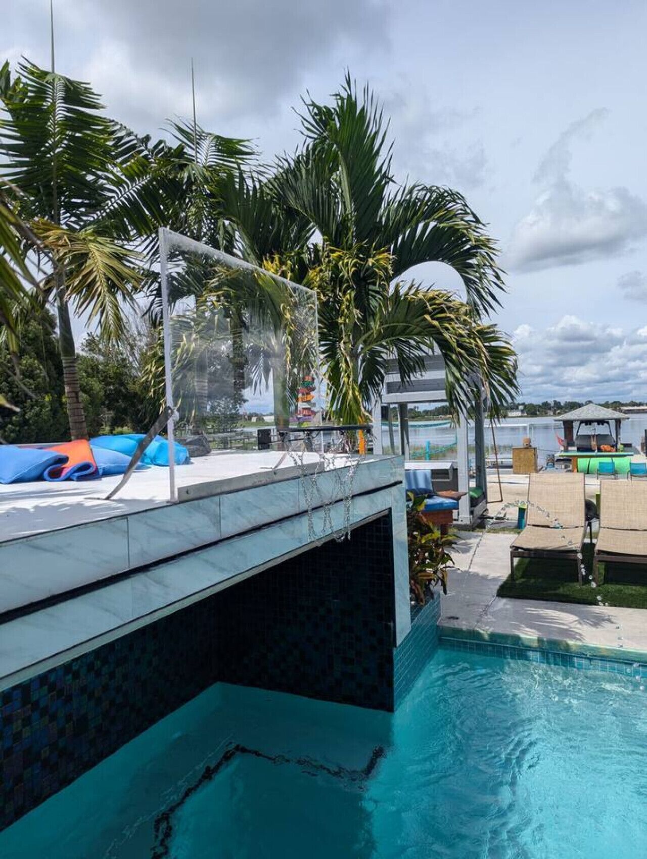 A swimming pool with a clear view of the water, surrounded by palm trees and a covered area with lounge chairs.