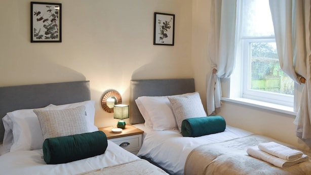 Habitación de hotel con dos camas, una mesita de noche con lámpara y una ventana con cortinas.