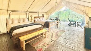 A tented accommodation with a bed, bench, table, and chairs.