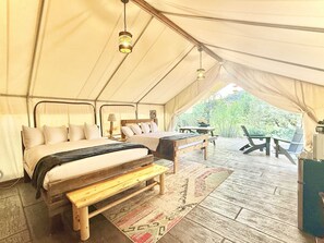 A tented accommodation with a bed, bench, table, and chairs.