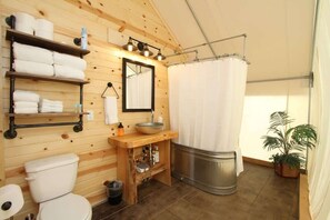 A wooden cabin bathroom with a toilet, sink, mirror, shelves with towels, and a shower curtain.