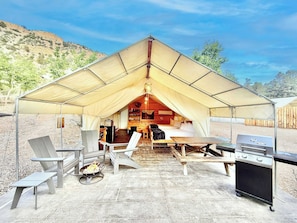 A tented accommodation with a dining area, a grill, and seating.