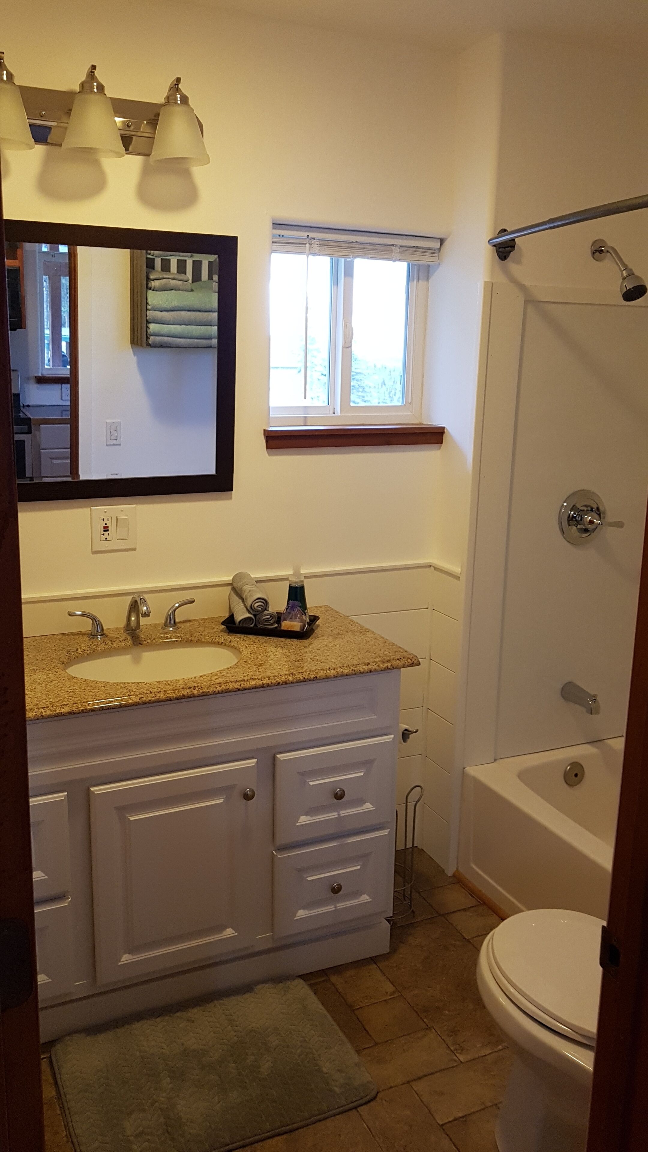 A bathroom with a sink, mirror, window, shower, and toilet.
