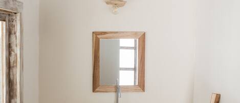 A bathroom with a wooden bench, a sink, a mirror, and a window with a wooden frame.