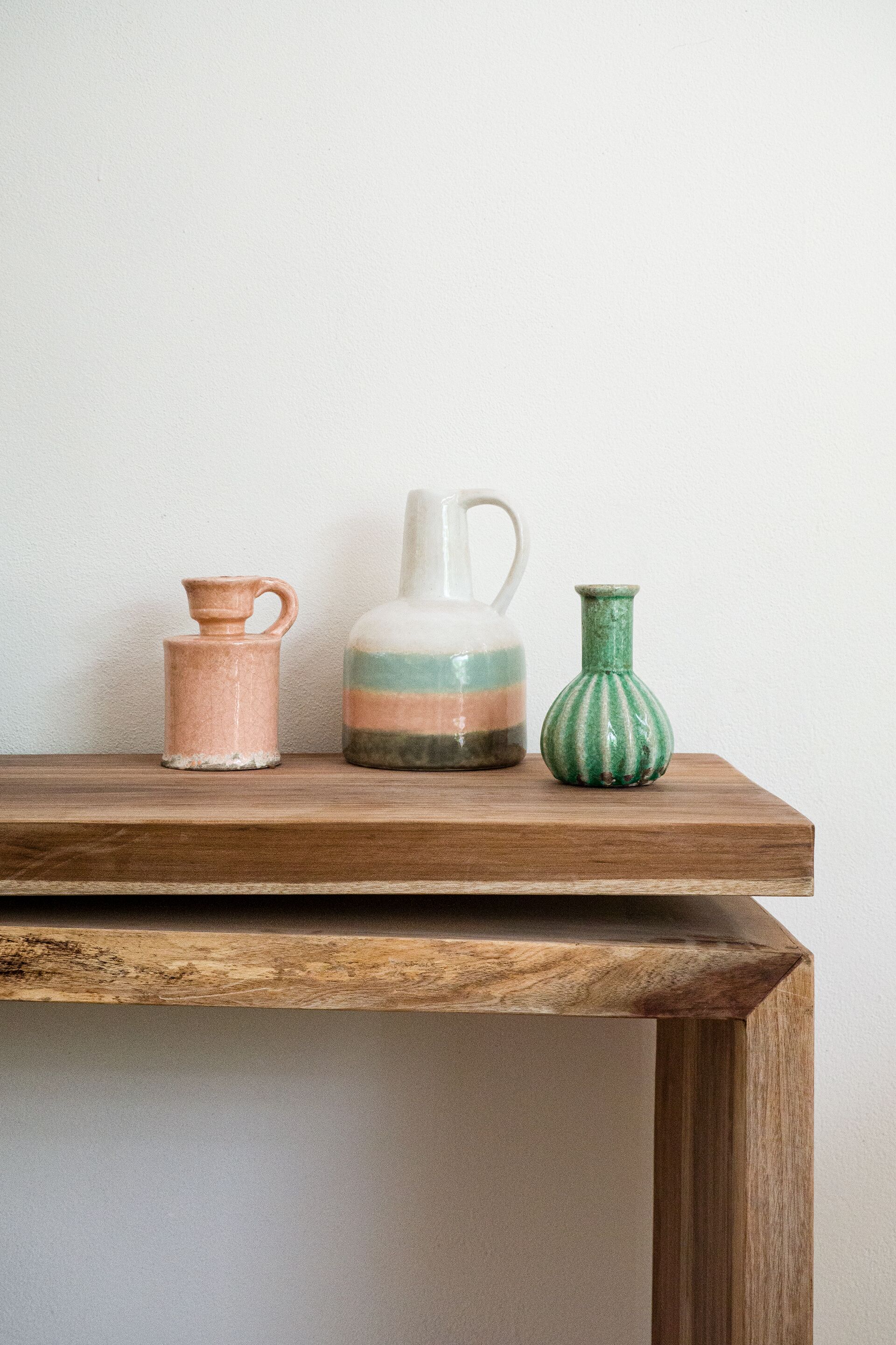 A wooden shelf with three ceramic vases of different shapes and colors.