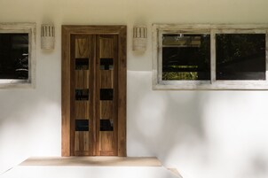 A room with a wooden door, two windows, and a light fixture on the wall.