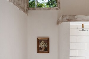 Um quadro emoldurado com flores numa parede, uma janela e uma parede com azulejos.