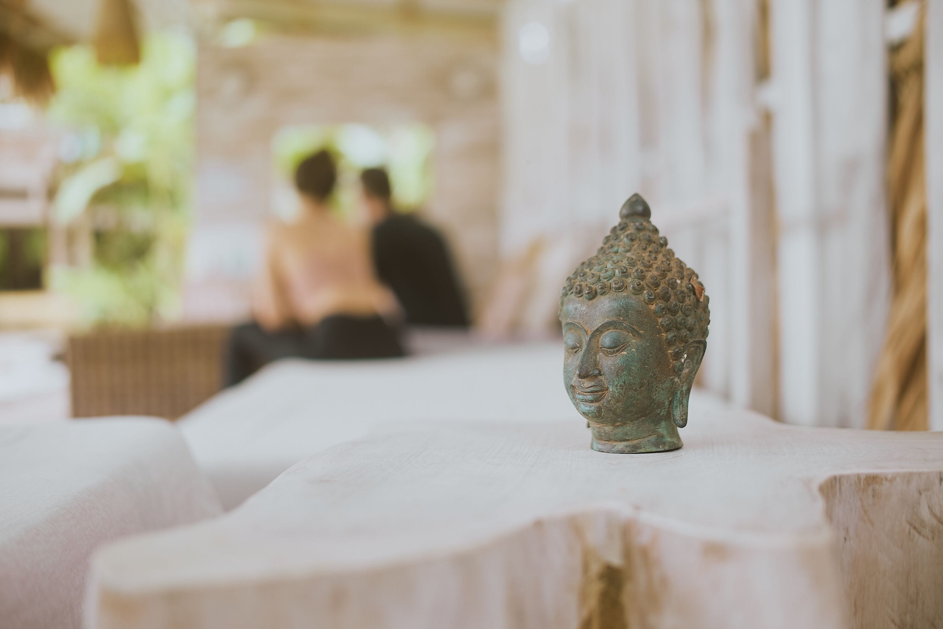 A Buddha statue on a table in a room with a blurred background of people.