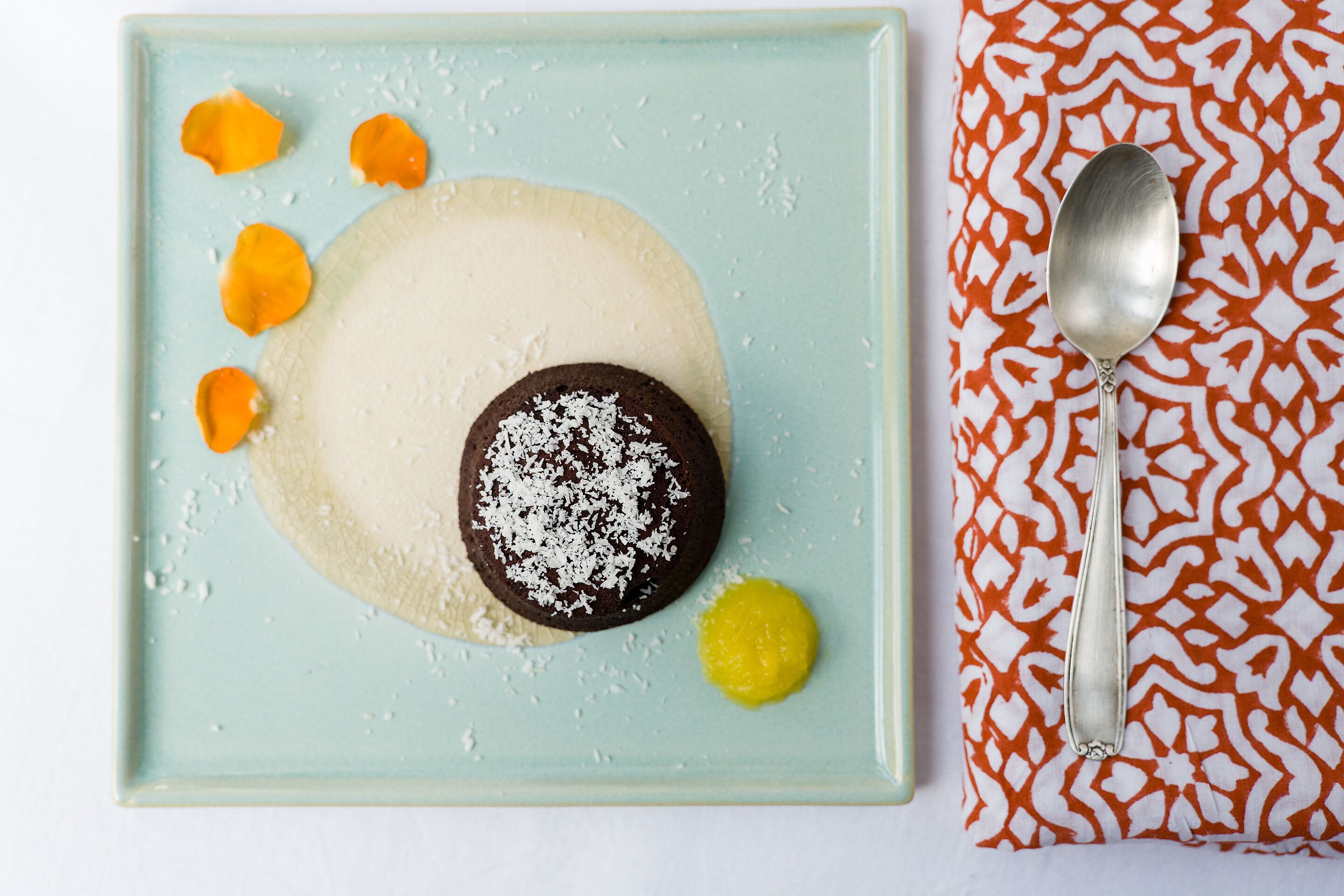 Een nagerechtenbord met een chocoladebedekte lekkernij, oranjebloemen en een gele saus.