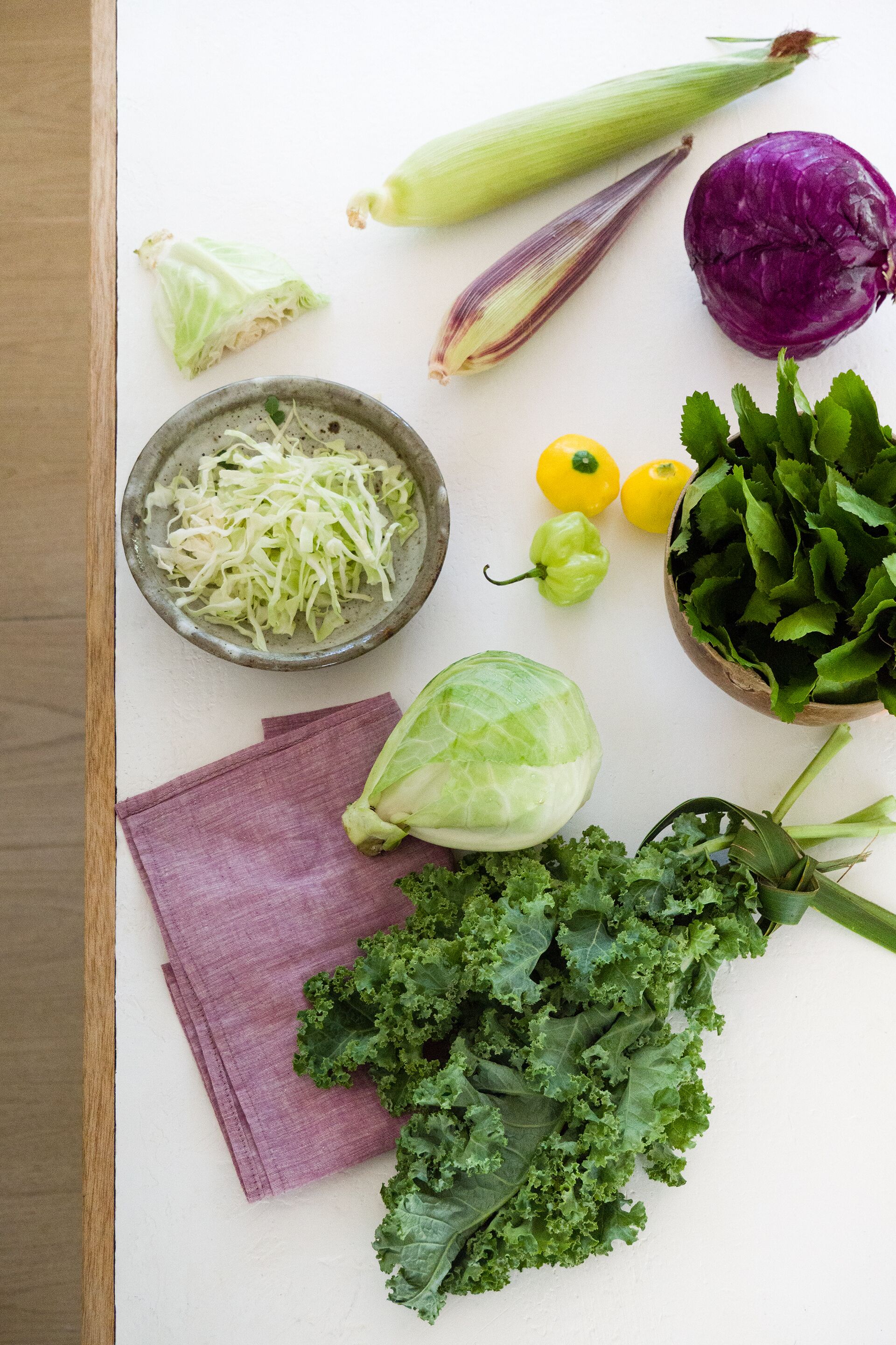A variety of vegetables including cabbage, kale, and bell peppers on a white surface.