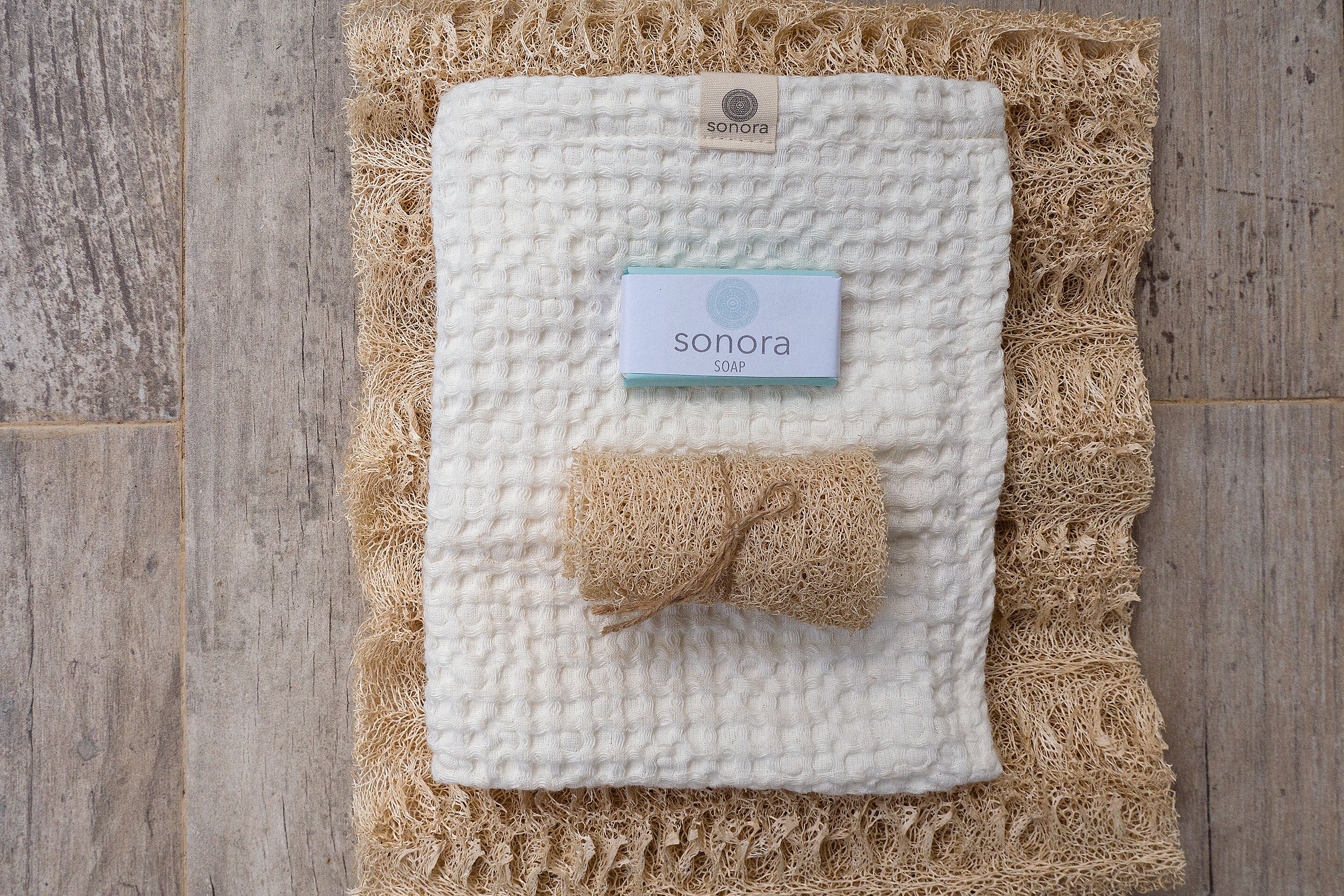 A white textured blanket with a Sonora soap label, placed on a woven mat.