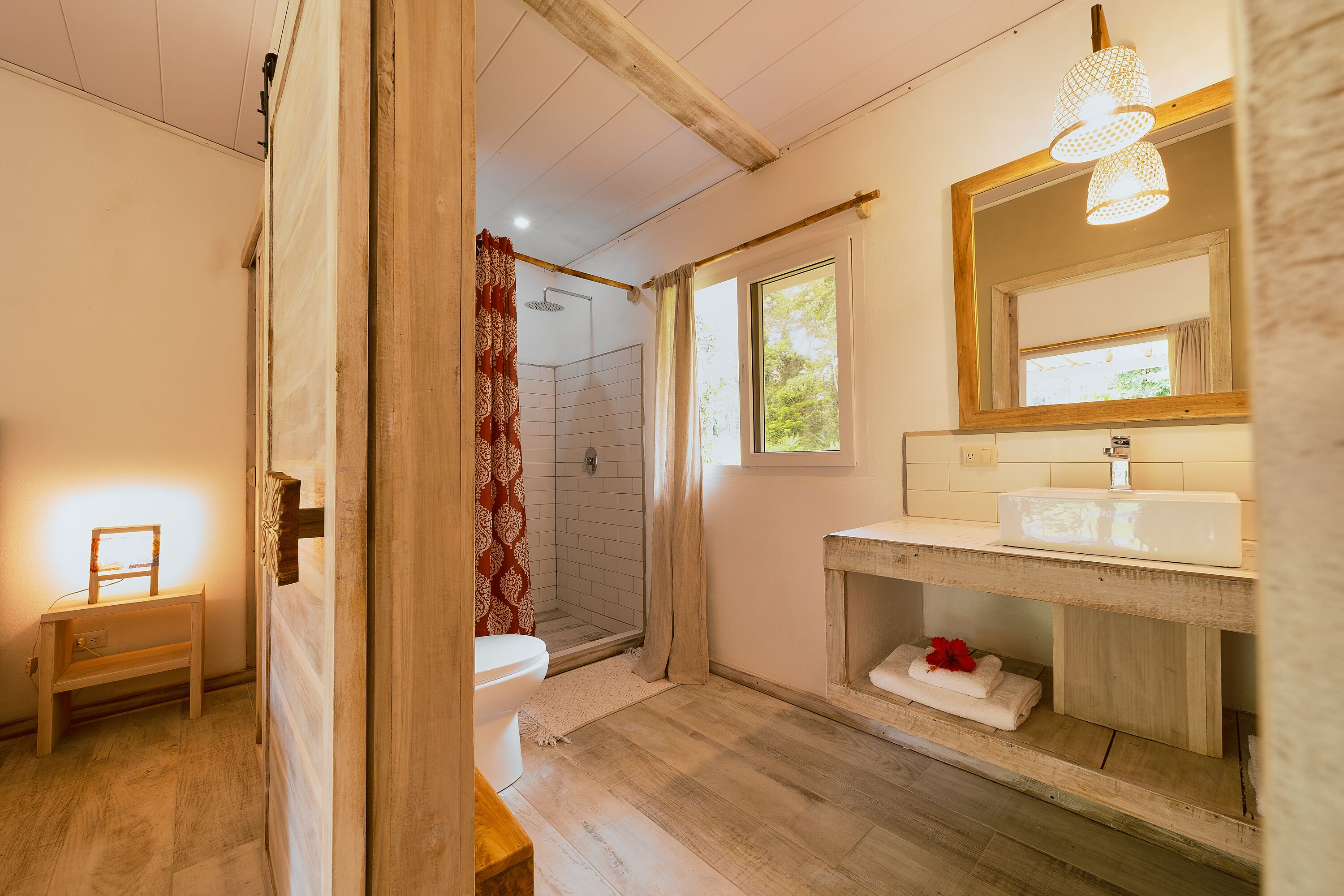Ein Badezimmer mit Holzboden, einem weißen Waschbecken, einem Spiegel und einer Duschkabine.