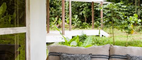 A seating area with a cushioned bench and patterned pillows, set against a backdrop of lush greenery and a pergola structure.