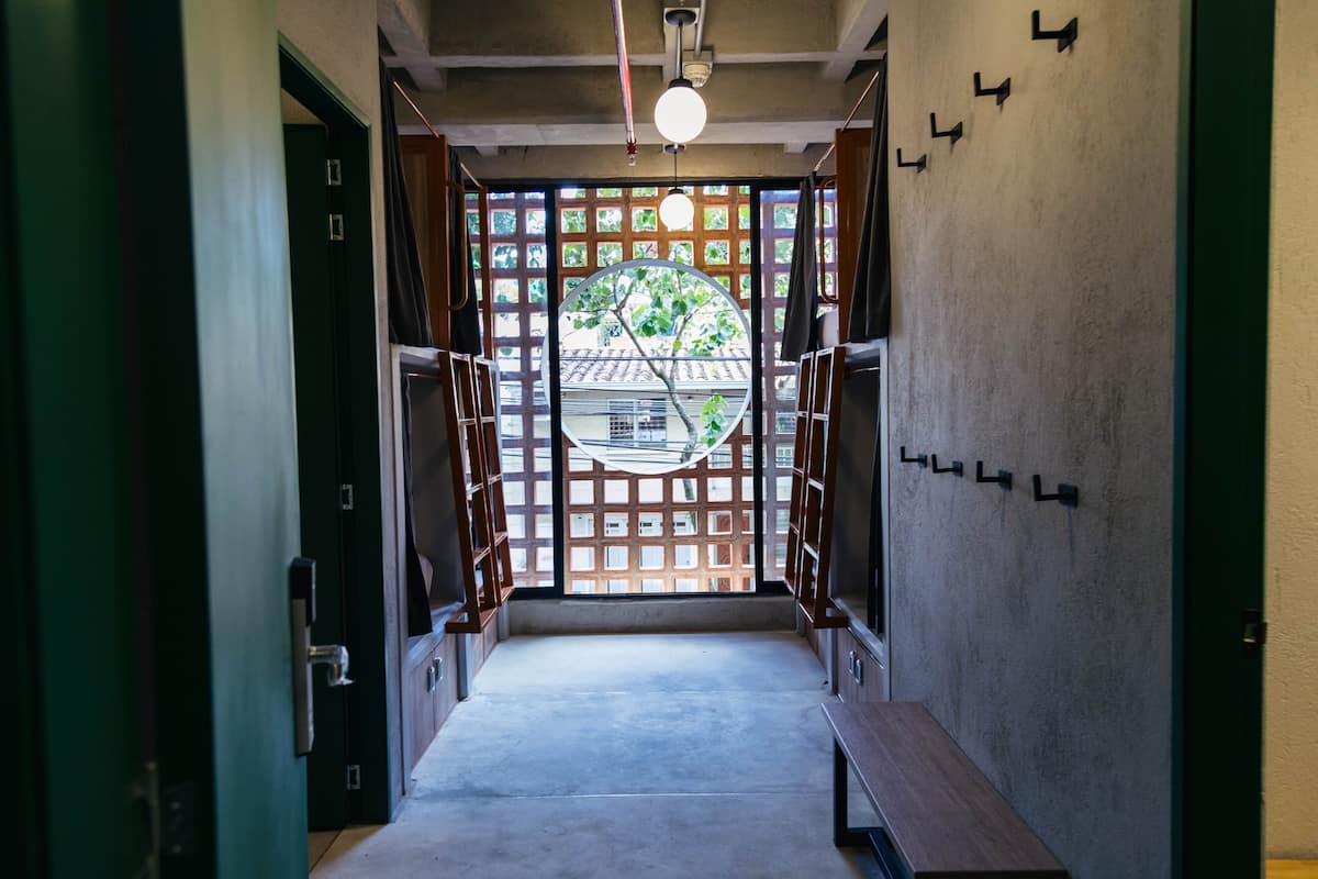 A hallway with a wooden bench, a circular window with a view of a building, and a ceiling light fixture.