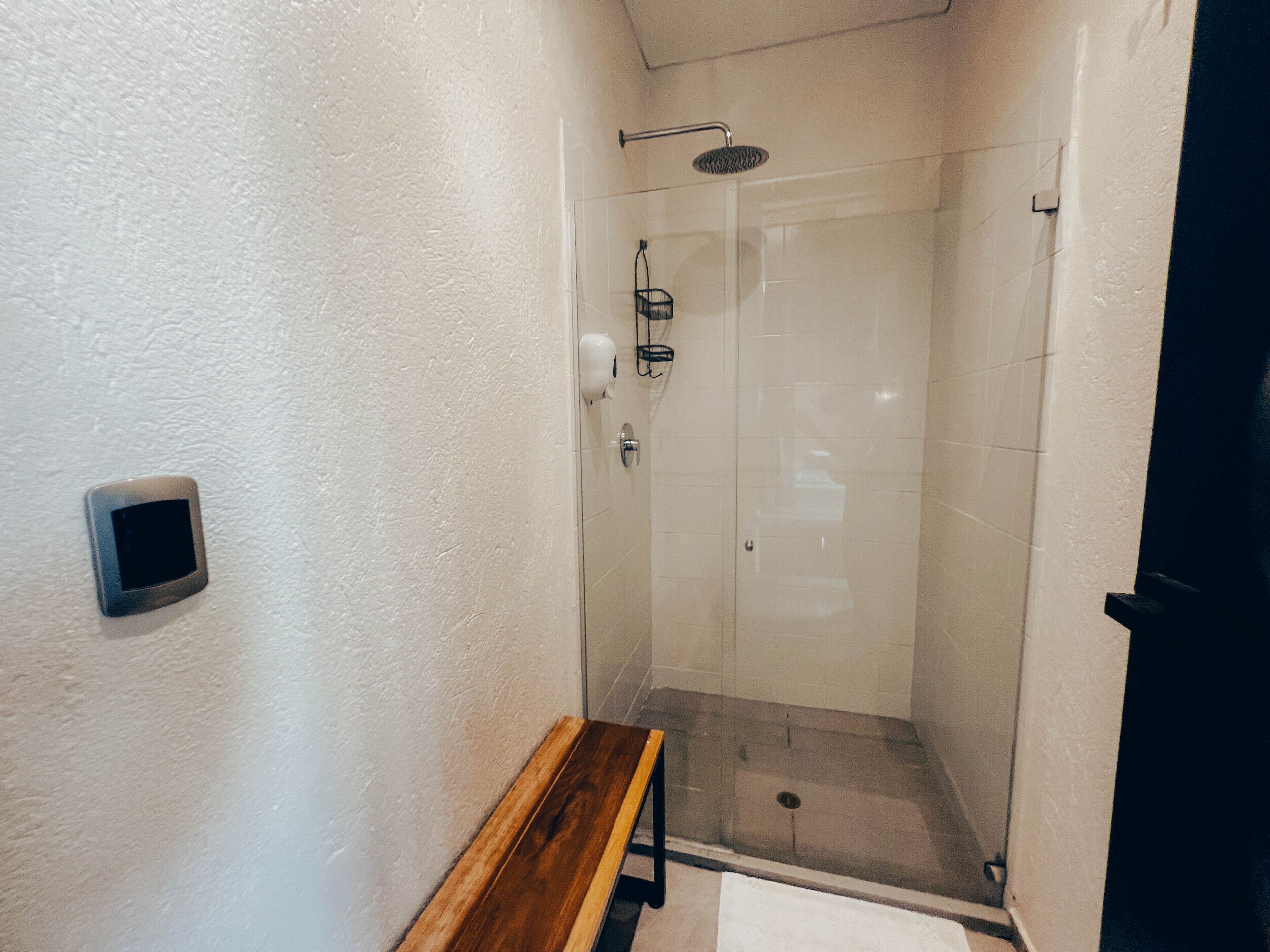 A glass-enclosed shower with a bench and a soap dispenser on the wall.