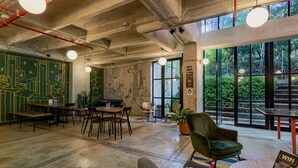 A modern workspace with exposed ceilings, large windows, and a green mural. - Viajero Hostel Medellin (Medellín)