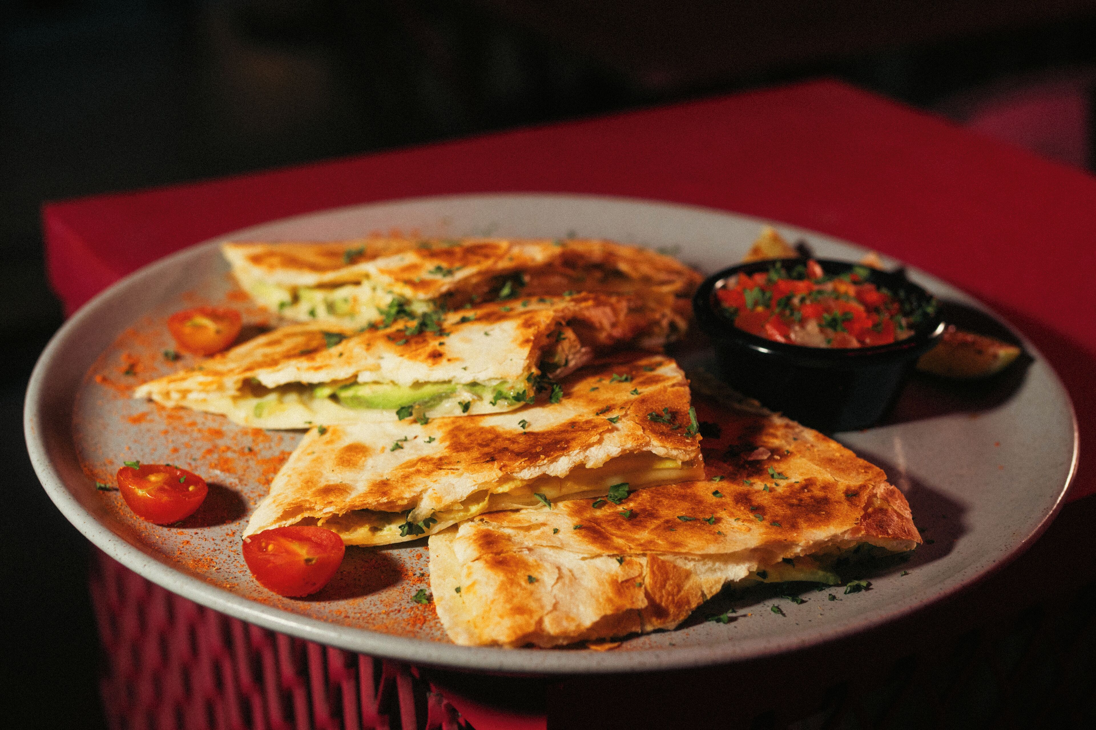 Un plato de quesadillas con tomates y una porción de salsa.