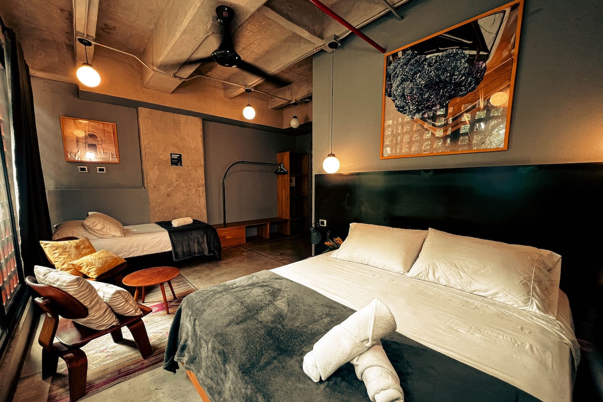 A hotel room with a large bed, a bench, a desk, and a ceiling fan.