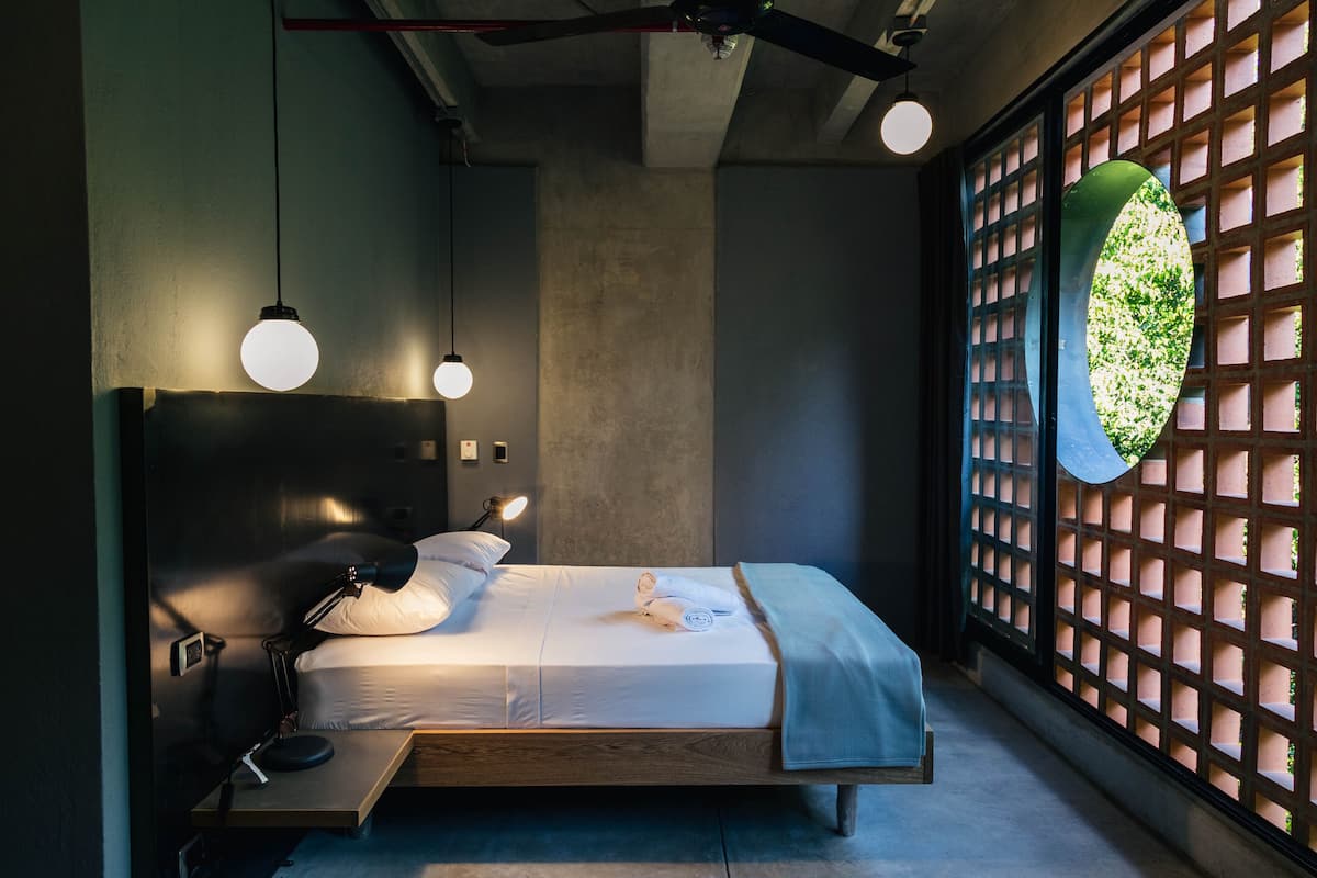 A modern bedroom with a wooden bed, bedside lamps, and a view through a lattice window.