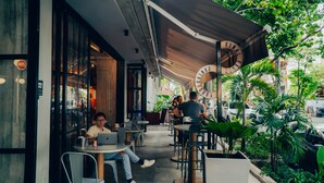 An outdoor cafe with tables and chairs, a sign reading "FOOD & DRINKS," and a view of the street with cars and greenery. - Viajero Hostel Medellin (Medellín)