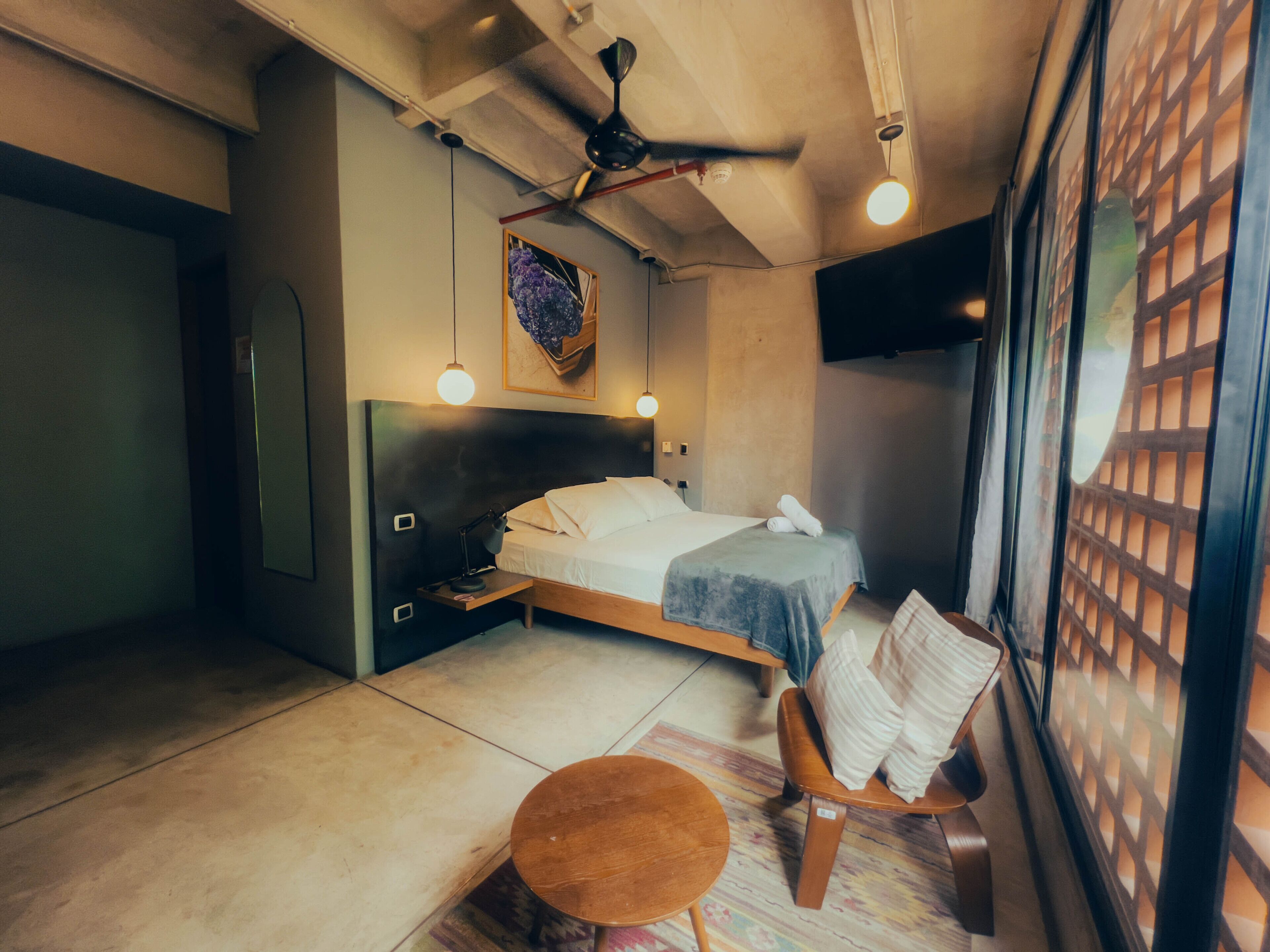 Een slaapkamer met een bed, nachtkastje, stoel en een klein rond tafeltje.