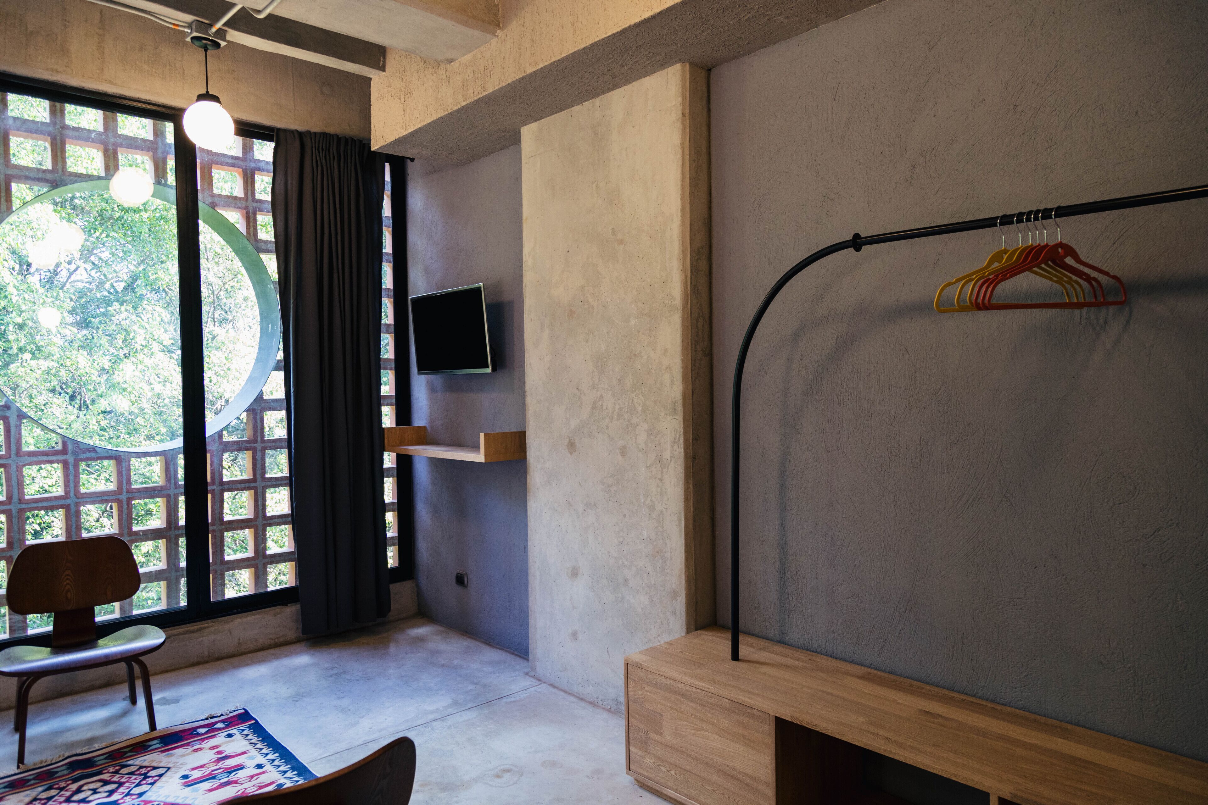 A room with a large window, a chair, a wooden bench, a TV, and a clothing rack.
