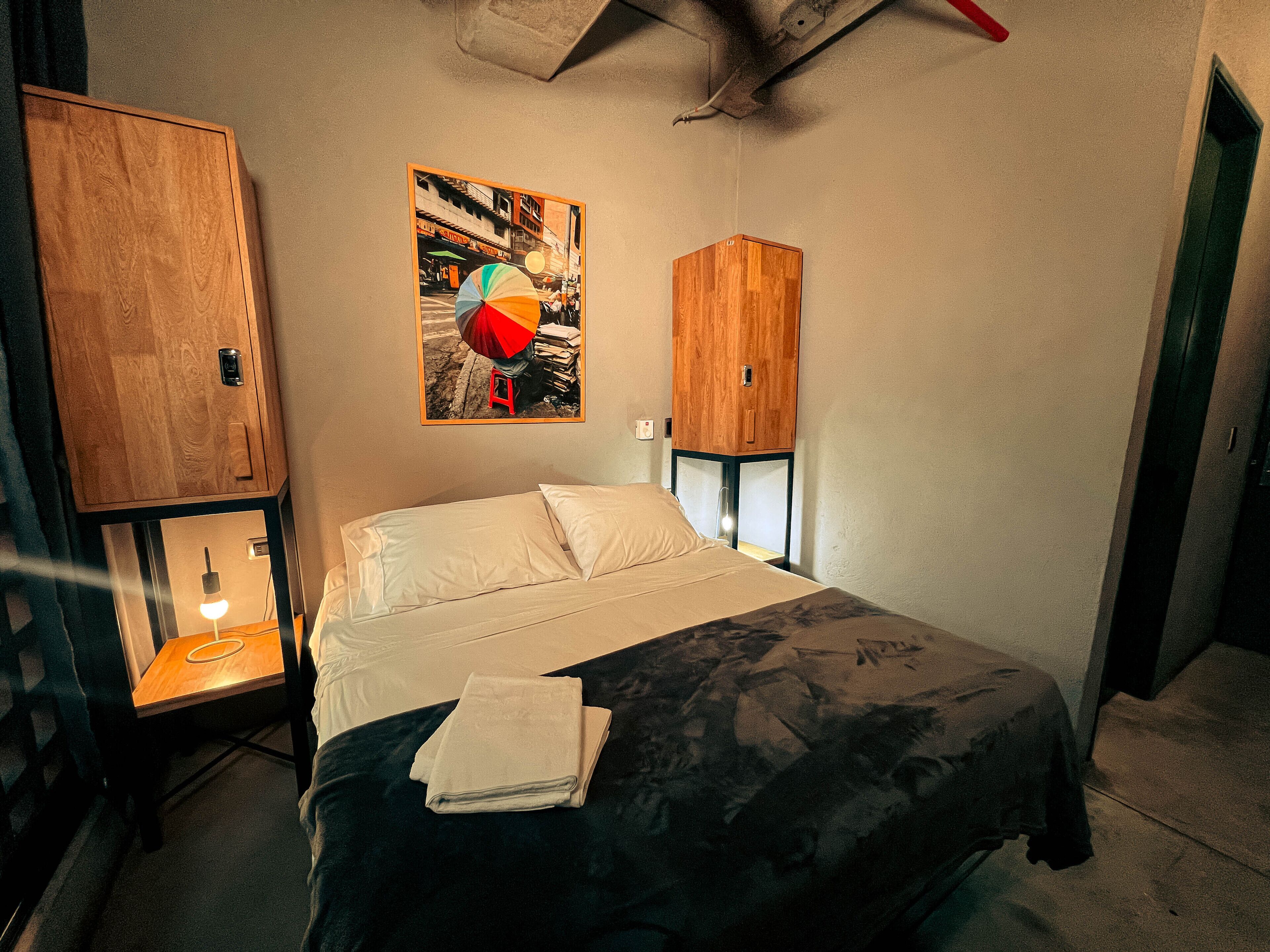 Una camera da letto con un letto, un armadietto in legno, uno sgabello e una mensola a muro.