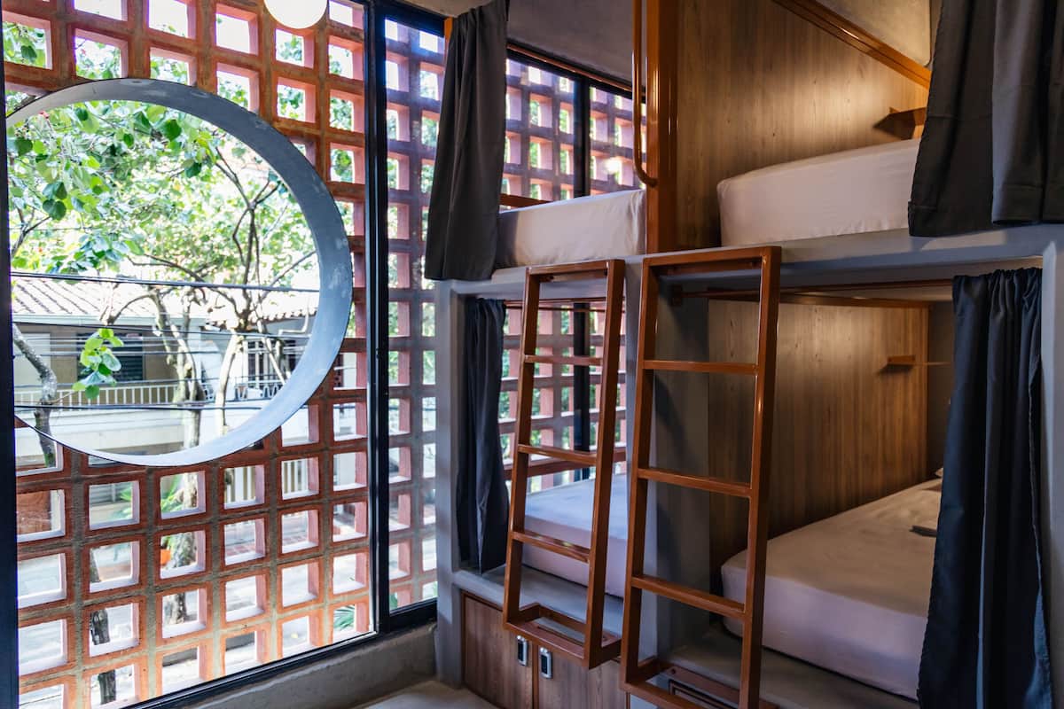 A bunk bed room with a wooden ladder, a circular mirror, and a view of a tree outside.