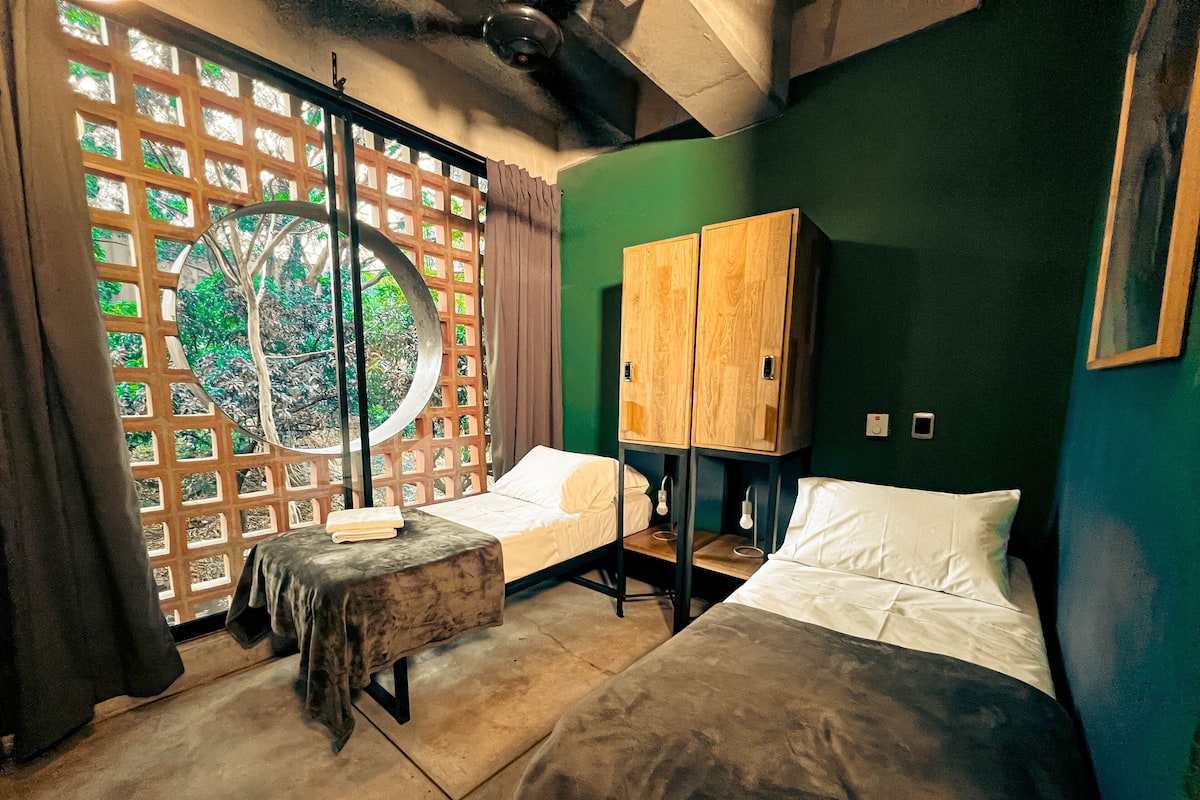 A room with two beds, a wooden wardrobe, and a window with a view of greenery.