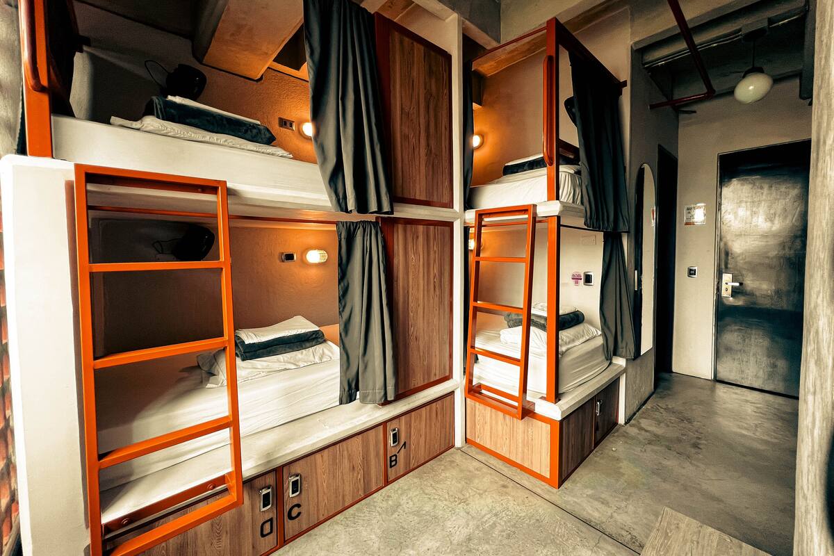 A bunk bed room with wooden frames, a small desk, and a door.