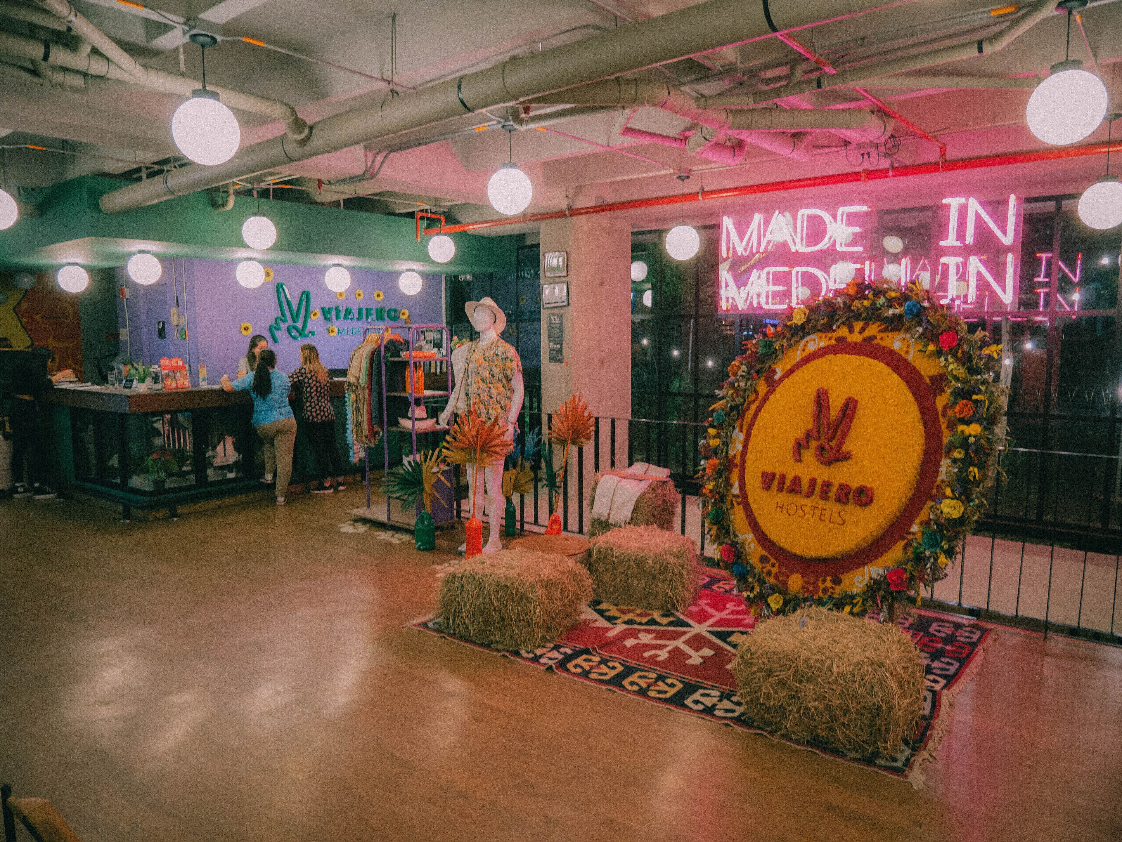 A hotel lobby with a central display featuring a mannequin, a reception desk, and a neon sign reading "MADE IN MEDALIN".