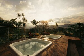 Een dak met twee jacuzzi's, omringd door tropische planten en een heldere lucht.