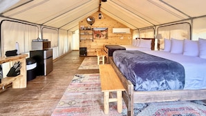 A tented accommodation with a bed, a table, a microwave, and a small kitchenette.