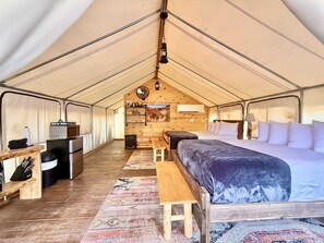A tented accommodation with a bed, a table, a microwave, and a small kitchenette.