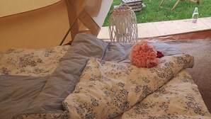 Een tent met een bed van binnen, een witte lantaarn, en twee comfortabele stoelen erbuiten.