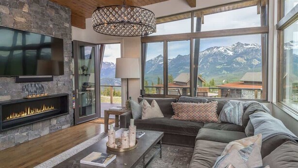 Un salon moderne doté d’une cheminée, de grandes fenêtres offrant une vue sur les montagnes et d’un coin salon confortable.