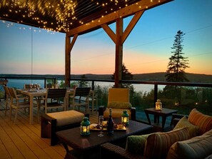 An outdoor deck with wooden furniture, string lights, and a view of the water and hills. - Whitecaps Summit Beach House (Riverport)