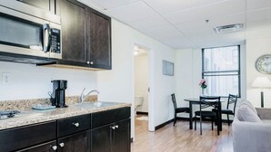 A modern kitchen with dark cabinets, a microwave, and a coffee maker. There is a dining area with a table and chairs.