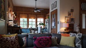 A cozy living room with a gray sofa, various patterned cushions, a ceiling fan, and a kitchen in the background. - open for summer 2020 (New Orleans)