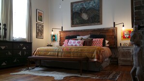 A bedroom with a wooden bed, patterned bedding, a large painting, and a statue. - open for summer 2020 (New Orleans)